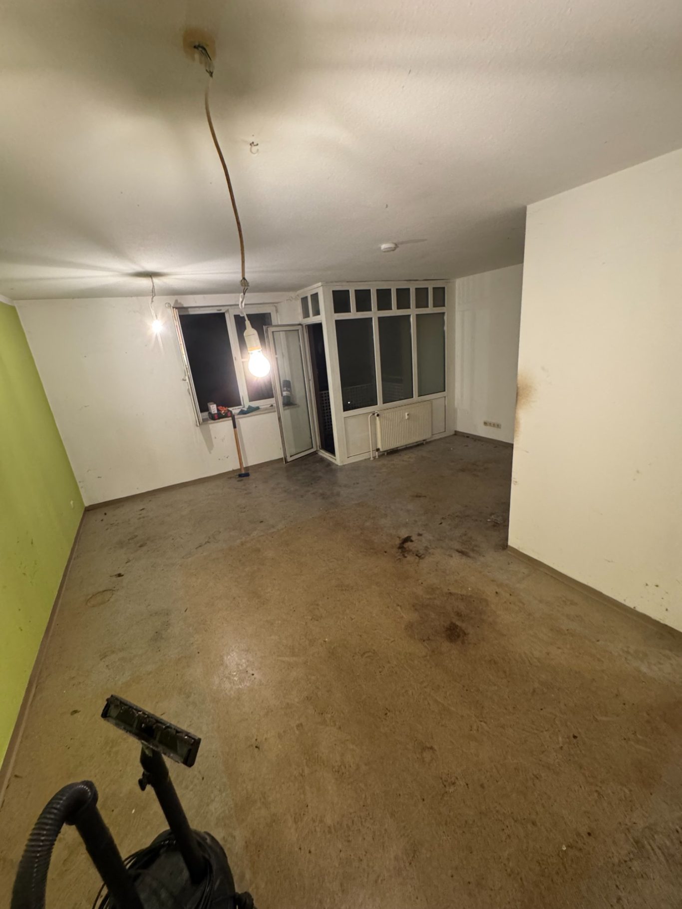 Leere, unverputzte Raum mit grauem Boden und grünem Akzent an einer Wand.